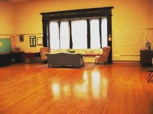 Channing Hall, First Unitarian Universalist Society of Albany, Albany — Located between the sanctuary and the Religious Education/Administration wing, is 30'x 45' and has a hardwood floor suitable for dancing. This social space can seat 100 for a meal, or 150 lecture-style in flexible seating. It has a sound system, and connects to the pantry, kitchen, and lobby. One end has a south-facing bay window and comfortable seating; the other has large panels on which are displayed art shows throughout the year.