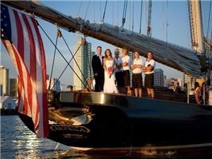 Yacht "America", San Diego — Bride & Groom pose with the yacht crew on the stern of the famous yacht "America", her lovely Gold Eagle glistening in the sunset and American flag flying proudly off the boom.