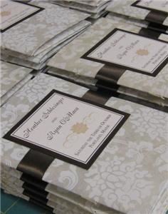 hullabaloo studios, Lisbon — Decorative ivory and cream paper adorns this booklet style invitation. Finished with a name plate and a wide satin chocolate ribbon that ties at the side. Invitation opens to reveal a hand-sewn booklet that contains all of the information the guest will need from ceremony invitation, to directions to the church and reception. Pocket in the back holds the response card with pre-printed and stamped envelope. ©hullabaloo studios
