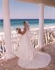 Photocraft By Tom Warriner, Destin — Bride on the balcony of a beach house in Destin, Florida. This stretch of beach along the Gulf of Mexico is known as the Emerald Coast because of the color of the water. The bride is wearing a stunning wedding dress and her wedding bouquet was design by a Destin florist.