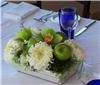 Sparks Florist, Sparks — This cool centerpiece features green cymbidium blossoms, white china mums, and shiny green apples in a flat ceramic tray.